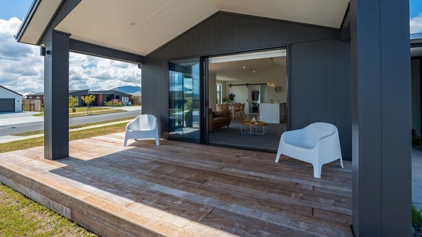Une maison moderne dotée d’un patio couvert comprenant deux chaises blanches et une terrasse en bois.