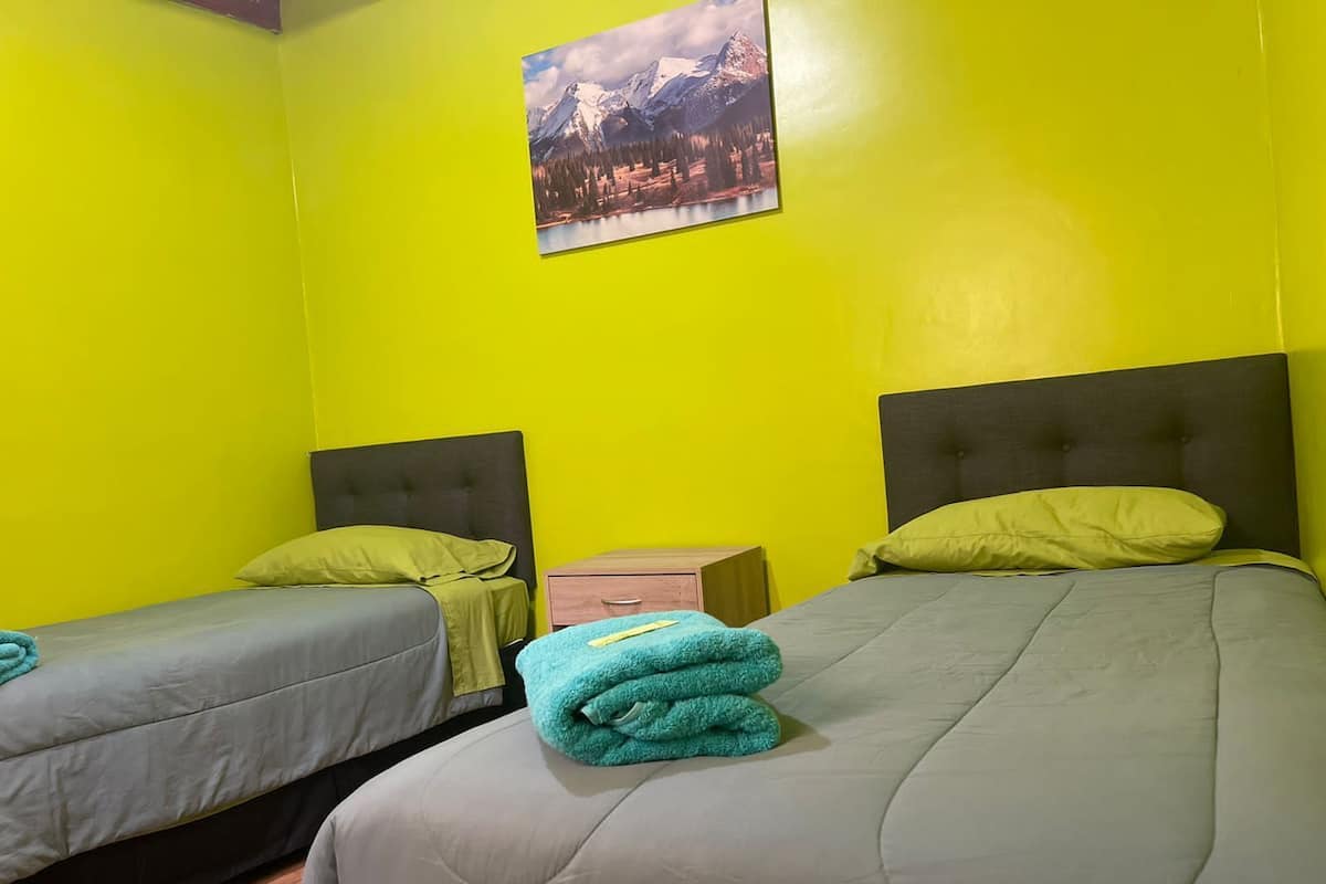 Une chambre avec deux lits, des murs d’un jaune vif et un tableau représentant un paysage de montagne au-dessus des lits.