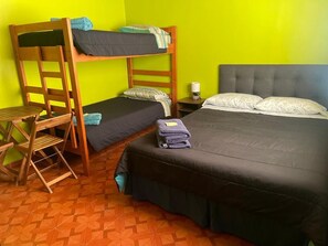 Ein Zimmer mit einem Etagenbett, einem Einzelbett, einem hölzernen Stuhl, einem kleinen Tisch und einem Nachttisch mit Lampe.