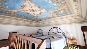 A room with two beds, a wooden bench, a ceiling with ornate designs, and a nightstand with a lamp. - Eucalipti 2 - Apartment (Porto Azzurro)