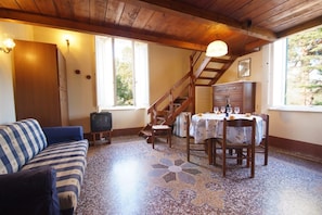 A cozy room with a wooden ceiling, a sofa, a dining table with chairs, a staircase, and a window with a view of trees. - Eucalipti 2 - Apartment (Porto Azzurro)