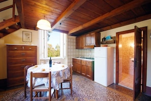 A kitchen with wooden cabinets, a dining table with chairs, a window, and a door leading to a bathroom. - Eucalipti 2 - Apartment (Porto Azzurro)