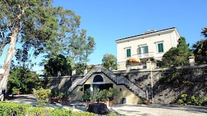 A building with a stone staircase leading to a balcony, surrounded by greenery. - Eucalipti 2 - Apartment (Porto Azzurro)