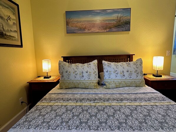 Una cama con ropa de cama floral, dos lámparas de noche, un cabecero de madera y un cuadro de una playa en la pared.