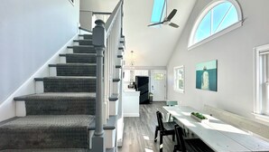 A modern kitchen with a central island, a dining area with a long table and chairs, and a staircase with a railing.