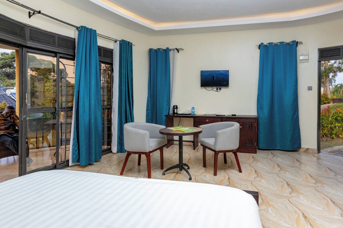 A hotel room with a bed, two chairs, a small table, a TV, and a desk with a computer.
