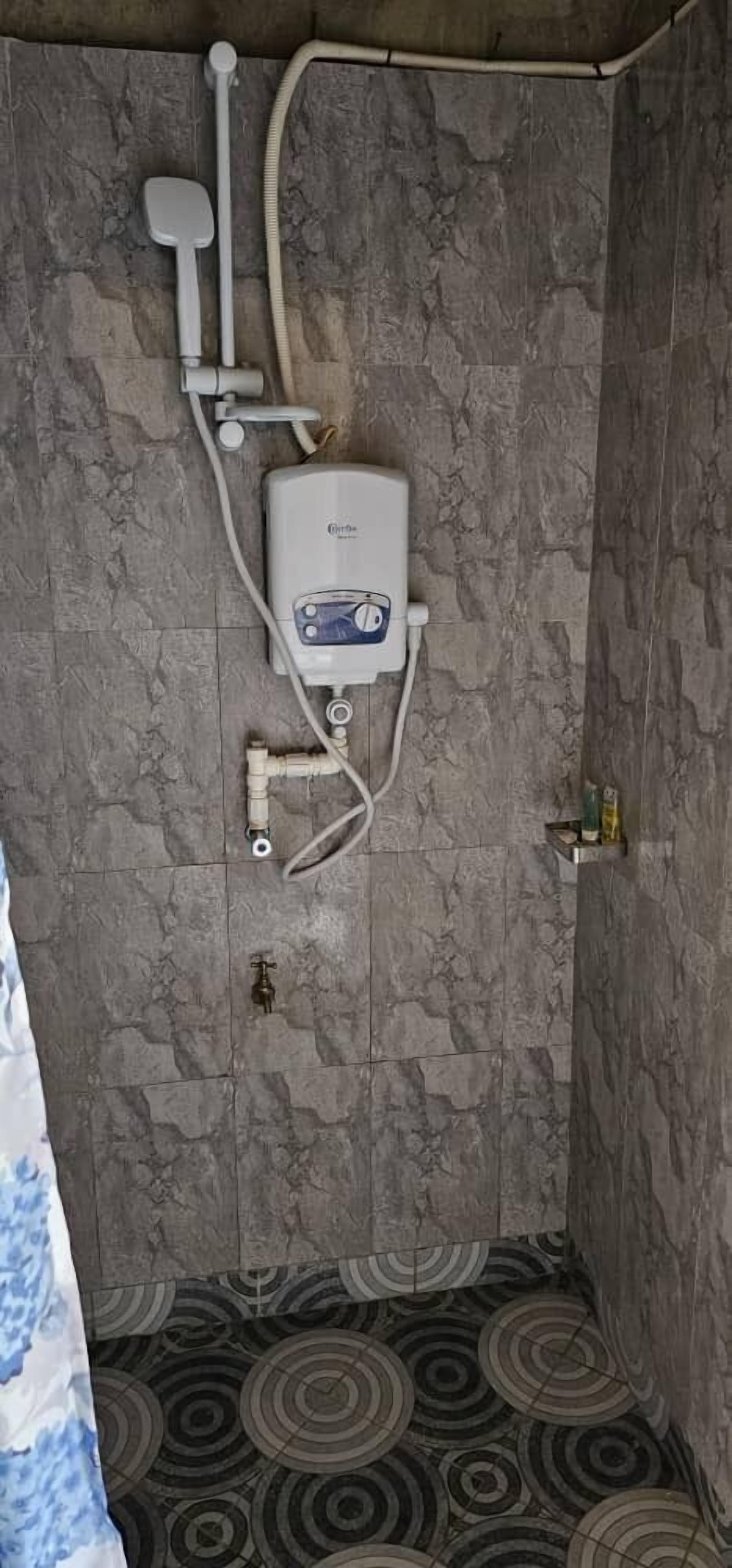 A shower area with a built-in water heater, a handheld showerhead, and a wall-mounted faucet.