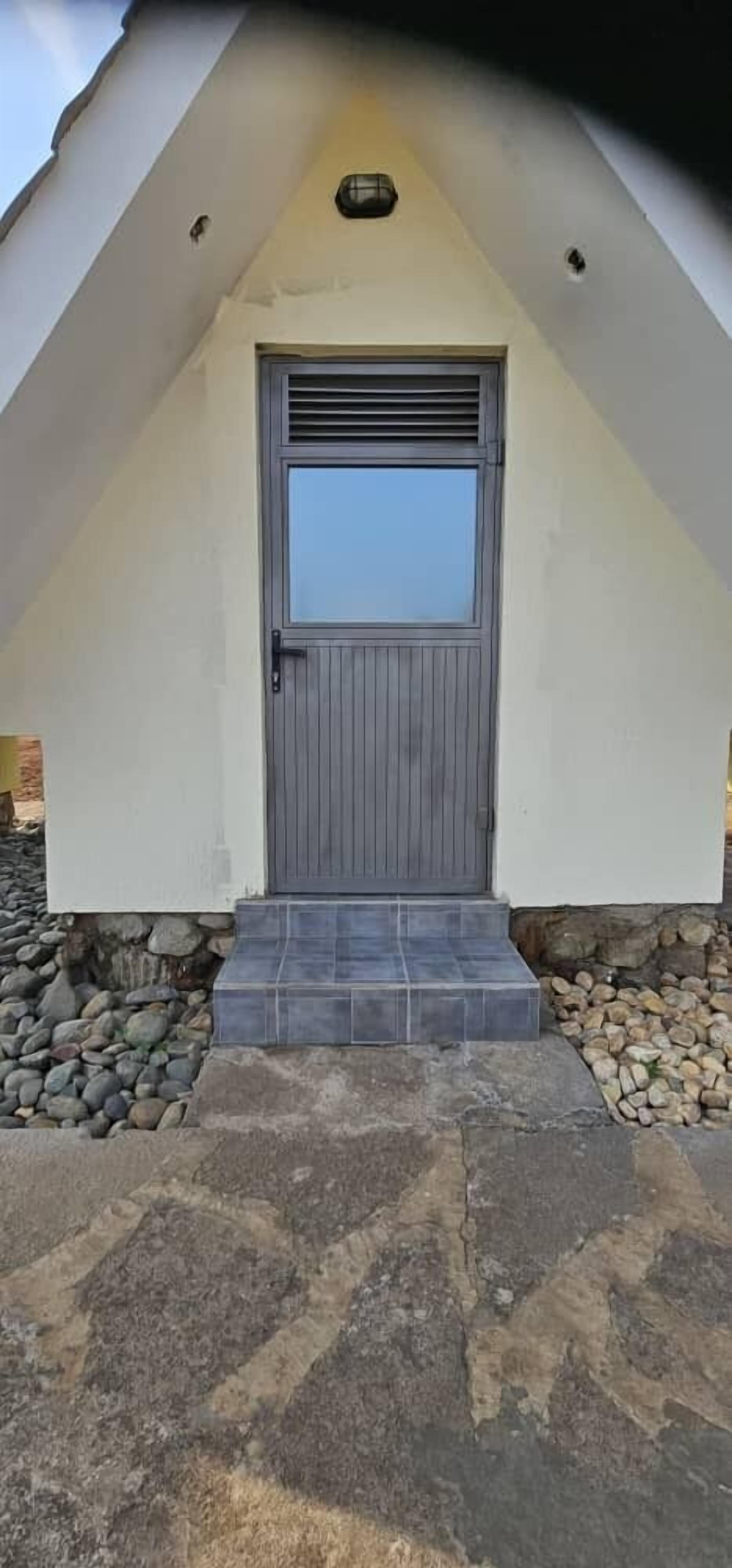 Un edificio moderno con techo triangular, una puerta gris y un pequeño conjunto de escalones de piedra que conducen a la entrada.
