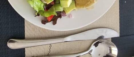 Un plato con ensalada, un pastel horneado y una patata sobre una mesa con posavasos.