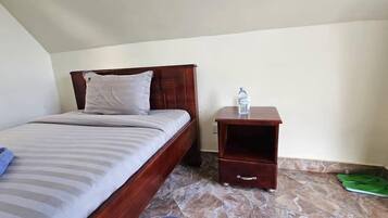A single bed with a wooden headboard and a nightstand with a water bottle and slippers.