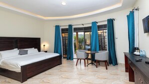 A bedroom with a bed, a desk, and a chair. There is a window with curtains. - Kaije Country Cottages (Fort Portal)