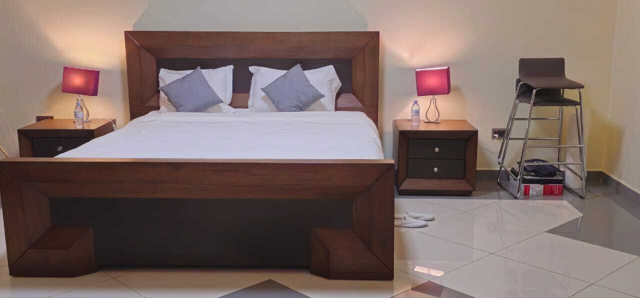 A wooden bed with a headboard, two bedside tables with lamps, a small stool, and a ladder.