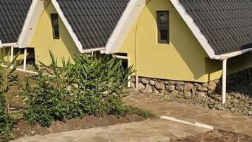 A row of yellow cottages with dark roofs and white trim, surrounded by greenery and a dirt path.