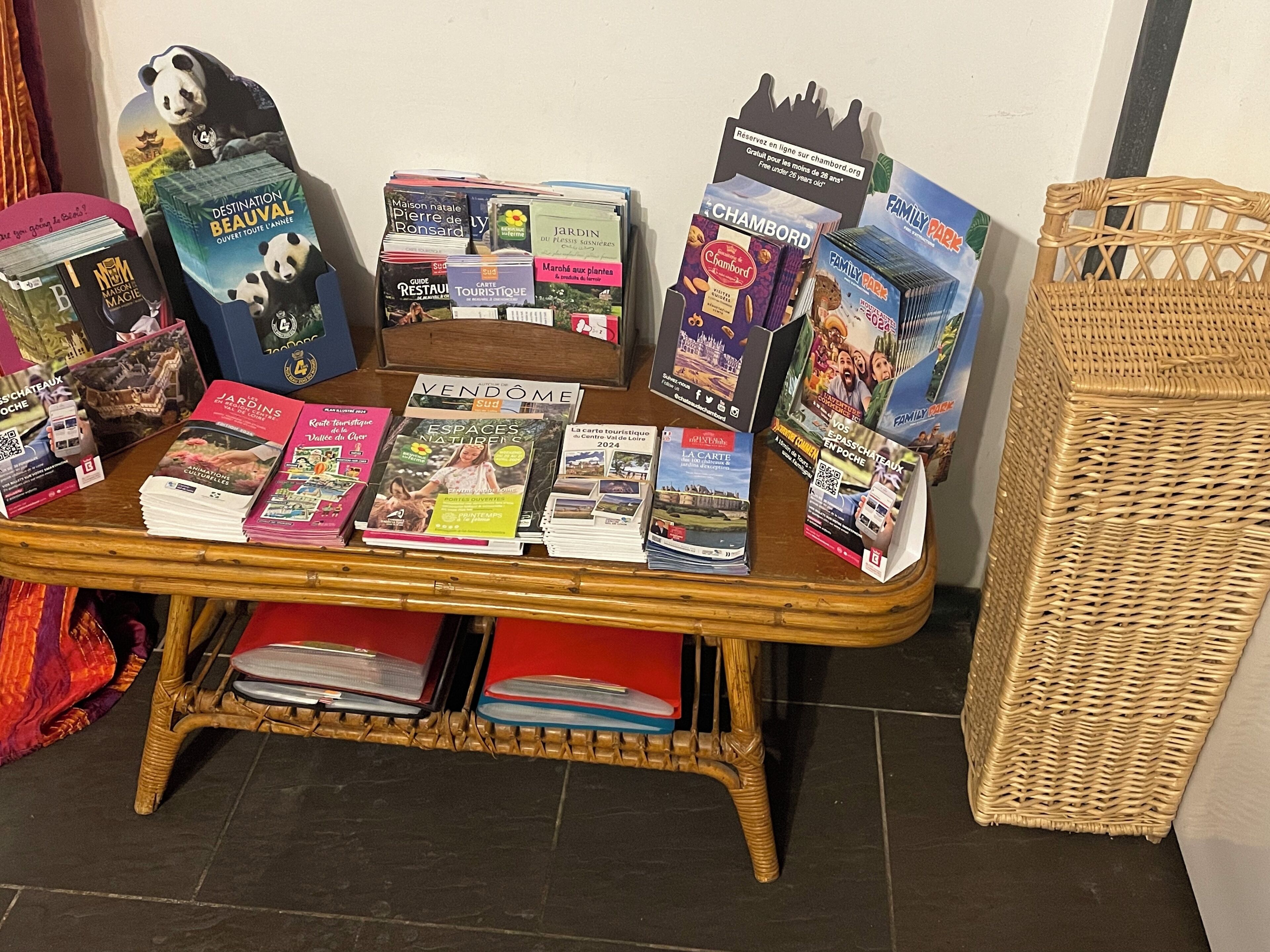 A table with various travel guides and maps, a wicker basket, and a wicker chair.