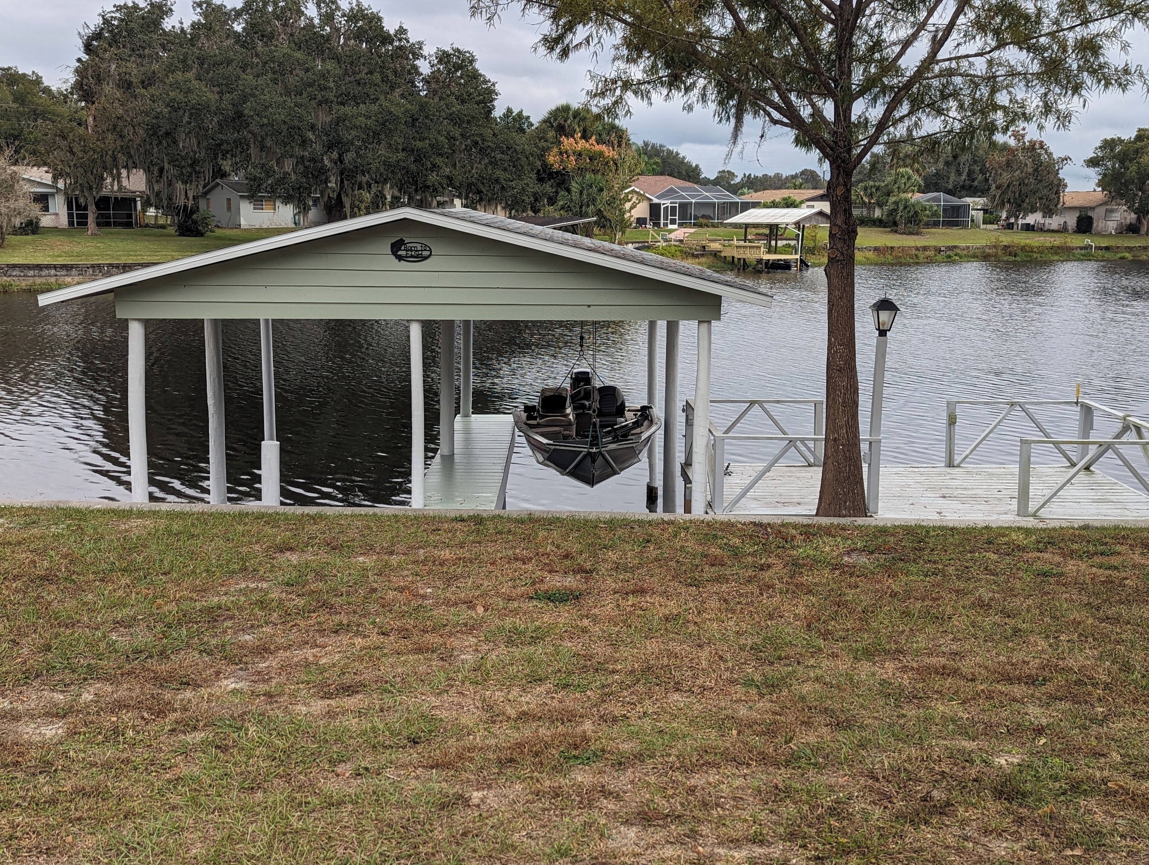 A covered boathouse with a swing seat by the water, a dock, and a lamp post.