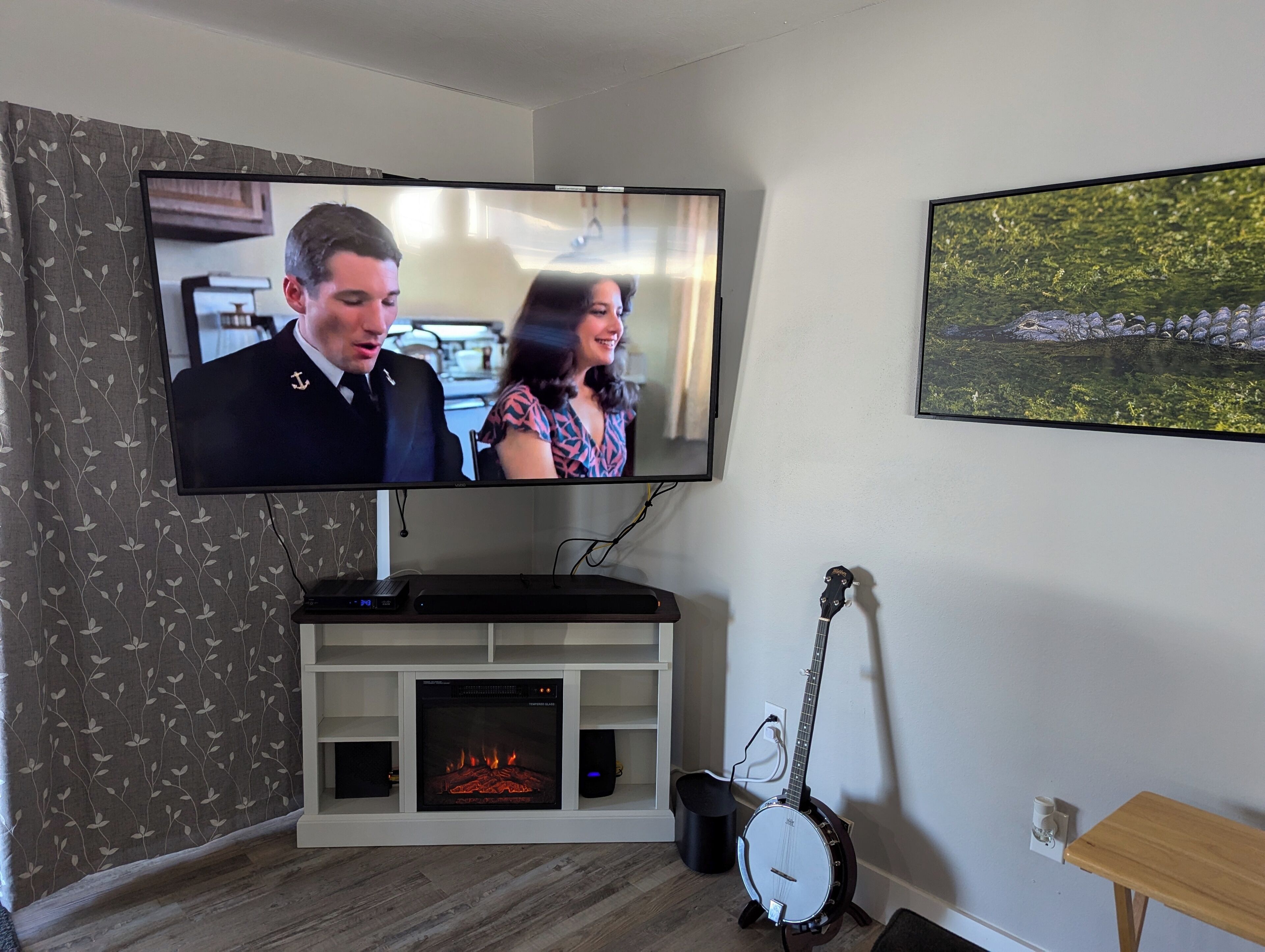 Una sala de estar con una televisión de pantalla plana montada en un mueble blanco, una chimenea, una guitarra y un cuadro enmarcado en la pared.