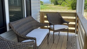 A covered porch with wicker furniture and a view of a natural landscape. - Sound Views! Brand New 3 bedroom (Kill Devil Hills)