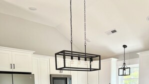 A modern kitchen with white cabinetry, stainless steel appliances, a central island with bar stools, and pendant lighting. - Sound Views! Brand New 3 bedroom (Kill Devil Hills)