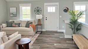 A living room with a beige sofa, a small round table, a white door, and a large window. - Sound Views! Brand New 3 bedroom (Kill Devil Hills)