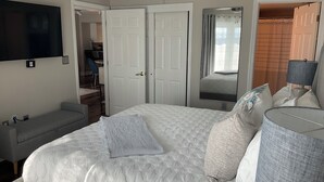 A bedroom with a large bed, a bedside table, a TV mounted on the wall, and a door leading to another room. - 7th Floor Beachfront Complex 2 BR 2B Beautifully furnished wFree Beach Service  (Fort Walton Beach)