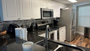 A modern kitchen with white cabinets, a black countertop, stainless steel appliances, and a wooden floor. - 7th Floor Beachfront Complex 2 BR 2B Beautifully furnished wFree Beach Service  (Fort Walton Beach)