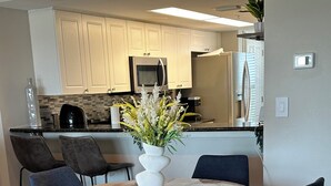 A dining area with a round table, four blue chairs, and a white vase with flowers. - 7th Floor Beachfront Complex 2 BR 2B Beautifully furnished wFree Beach Service  (Fort Walton Beach)