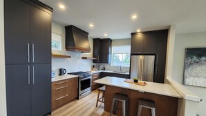 Une cuisine moderne avec des meubles de couleur sombre, des appareils électroménagers en acier inoxydable et un plancher en bois.