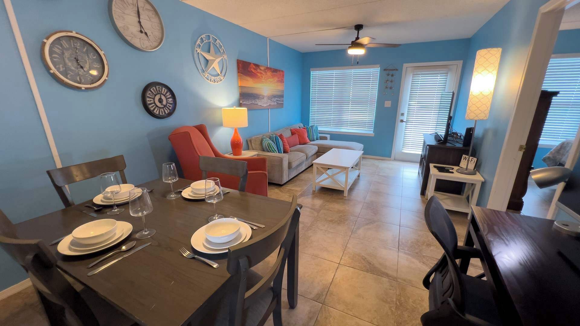 Un comedor con una mesa preparada para cuatro personas, un sofá y un televisor al fondo.