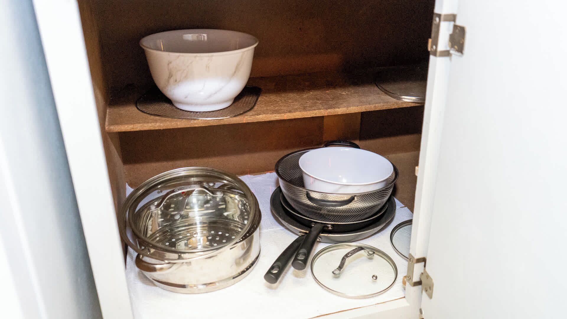 Un armario de cocina con diferentes utensilios de cocina, incluyendo una olla grande, un colador y un escurridor.