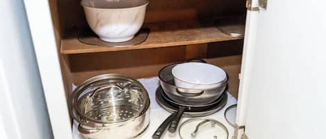Un armario de cocina con diferentes utensilios de cocina, incluyendo una olla grande, un colador y un escurridor.