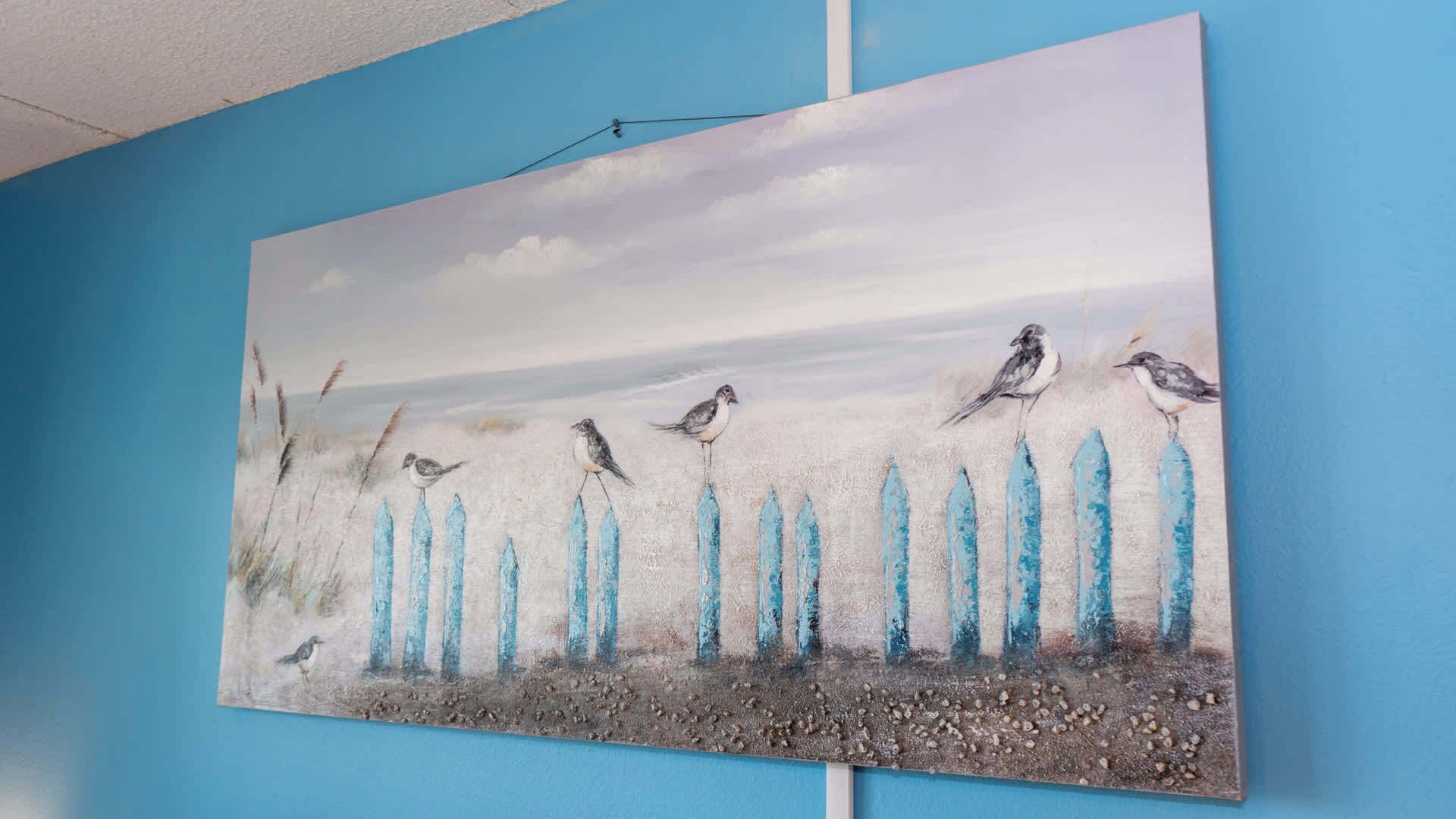 Una pintura de pájaros en una cerca frente a una pared azul.