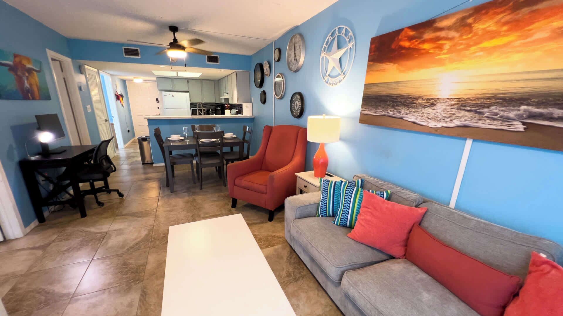 A living room with a gray sofa, red armchair, and a painting of a sunset.