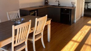 Une cuisine moderne avec des meubles de rangement de couleur sombre, une table à manger en bois et des chaises blanches.