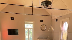 Un vaste espace de vie doté d’un plancher en bois, d’un grand canapé, d’une table à manger avec des chaises, d’un téléviseur fixé au mur et d’une fenêtre laissant entrer la lumière naturelle.