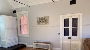 Une pièce dotée d’un plancher en bois, d’un banc blanc, d’une armoire blanche, d’une porte avec des panneaux de verre et d’une œuvre d’art représentant un vélo, accrochée au mur.