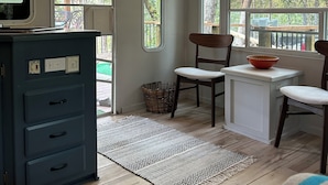 Um ambiente acolhedor com cozinha compacta, piso de madeira, tapete estampado e amplas janelas com vista para o exterior.