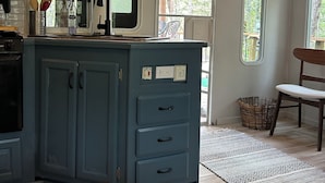 Uma cozinha compacta com uma ilha azul, micro-ondas e janela com vista para um jardim.