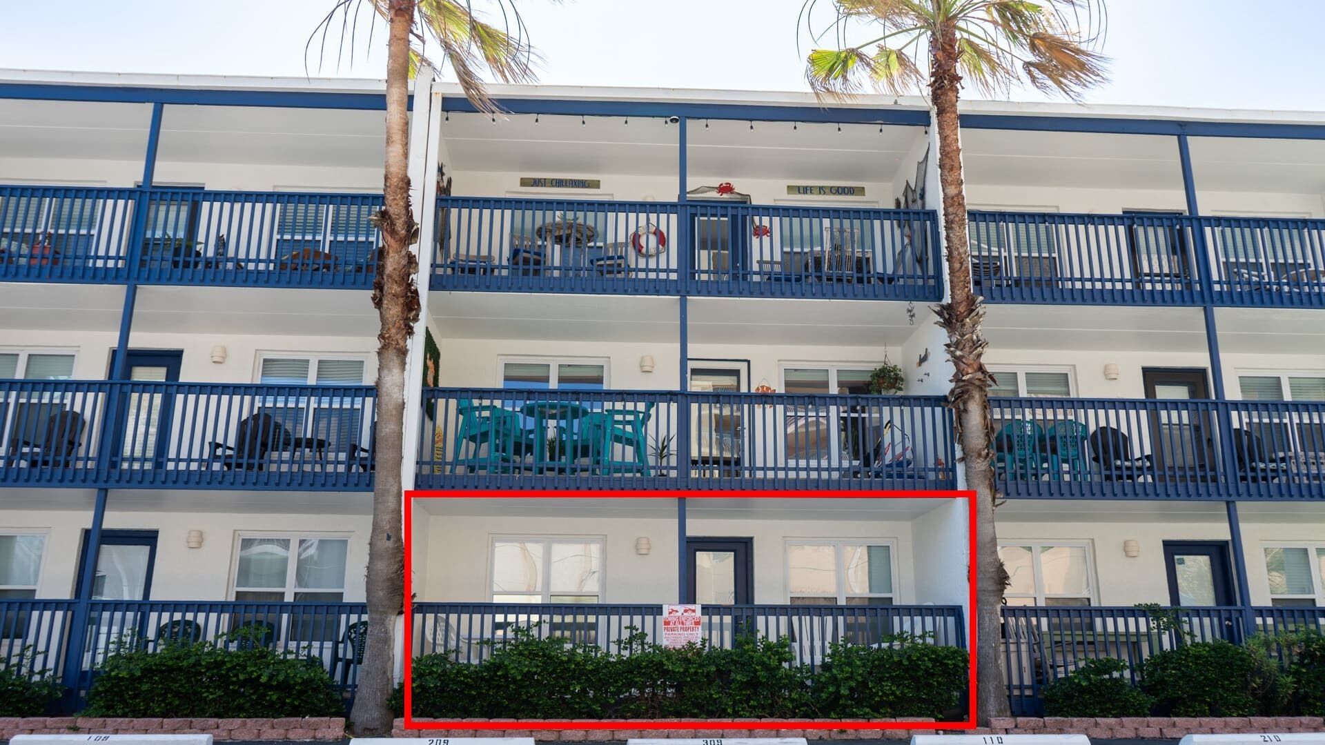 Een meerlaags hotel met balkons, palmbomen en een raam met rode omlijsting.