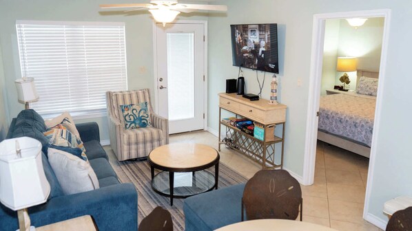 A living room with a sofa, armchair, coffee table, and a TV on a stand.