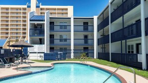 A pool area with a clear blue pool, surrounded by a low fence, and adjacent to a multi-story building with balconies. - Updated - Comfy Inside - Beach 50 Yards Away (South Padre Island)