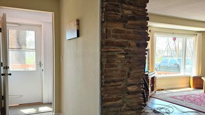 Un pasillo con un revestimiento de piedra en una pared, una puerta blanca y una alfombra que lleva a una habitación con vistas a coches estacionados afuera.