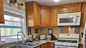 Una cocina con gabinetes de madera, un fregadero de acero inoxidable, un microondas, una estufa y un lavavajillas.