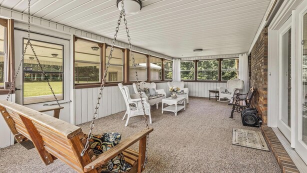 Eine überdachte Veranda mit weißen Korbmöbeln, einer Holzschaukel und einer Backsteinmauer.