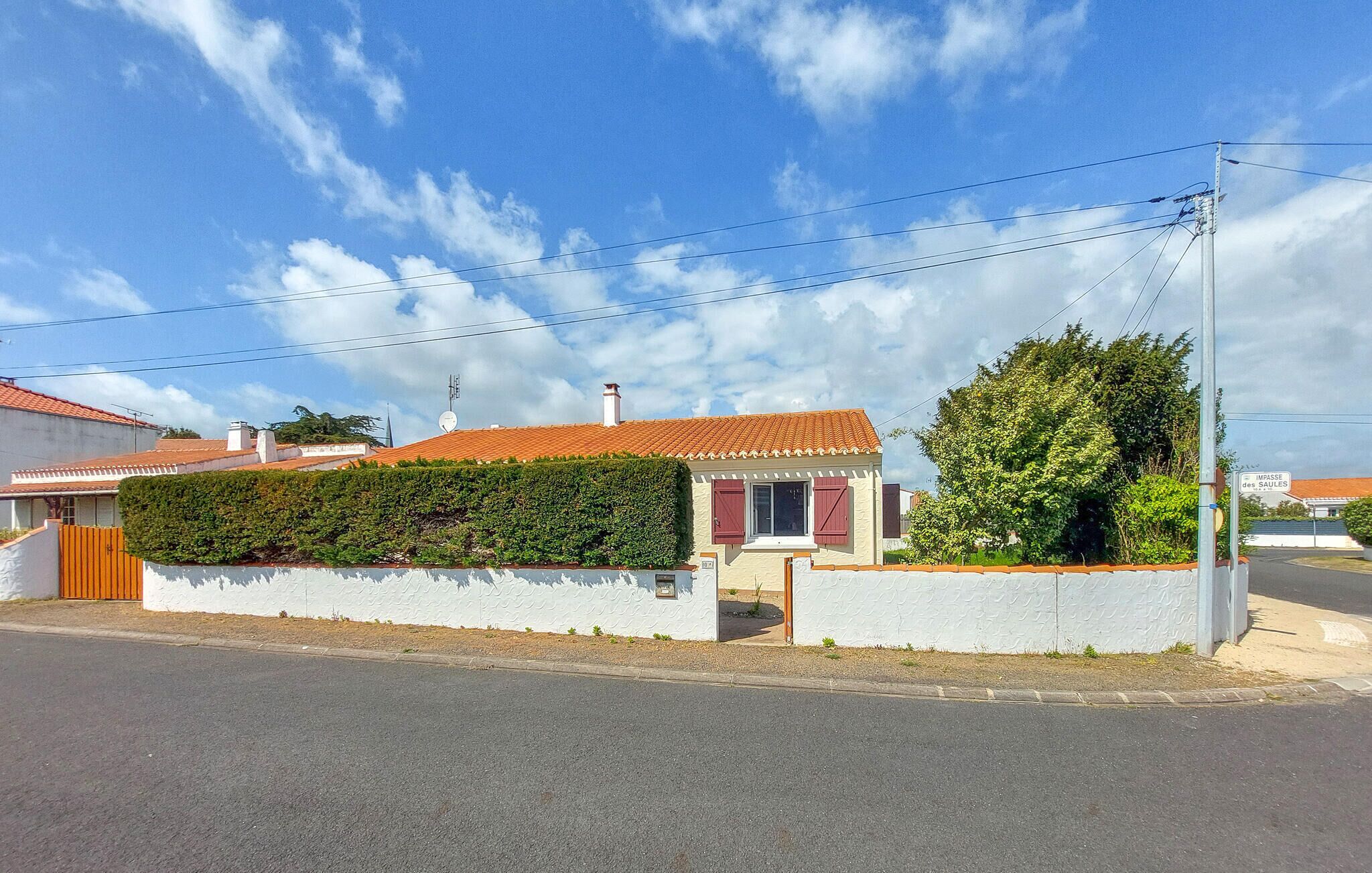 Una casa residencial con techo de tejas rojas, paredes blancas y un pequeño jardín.