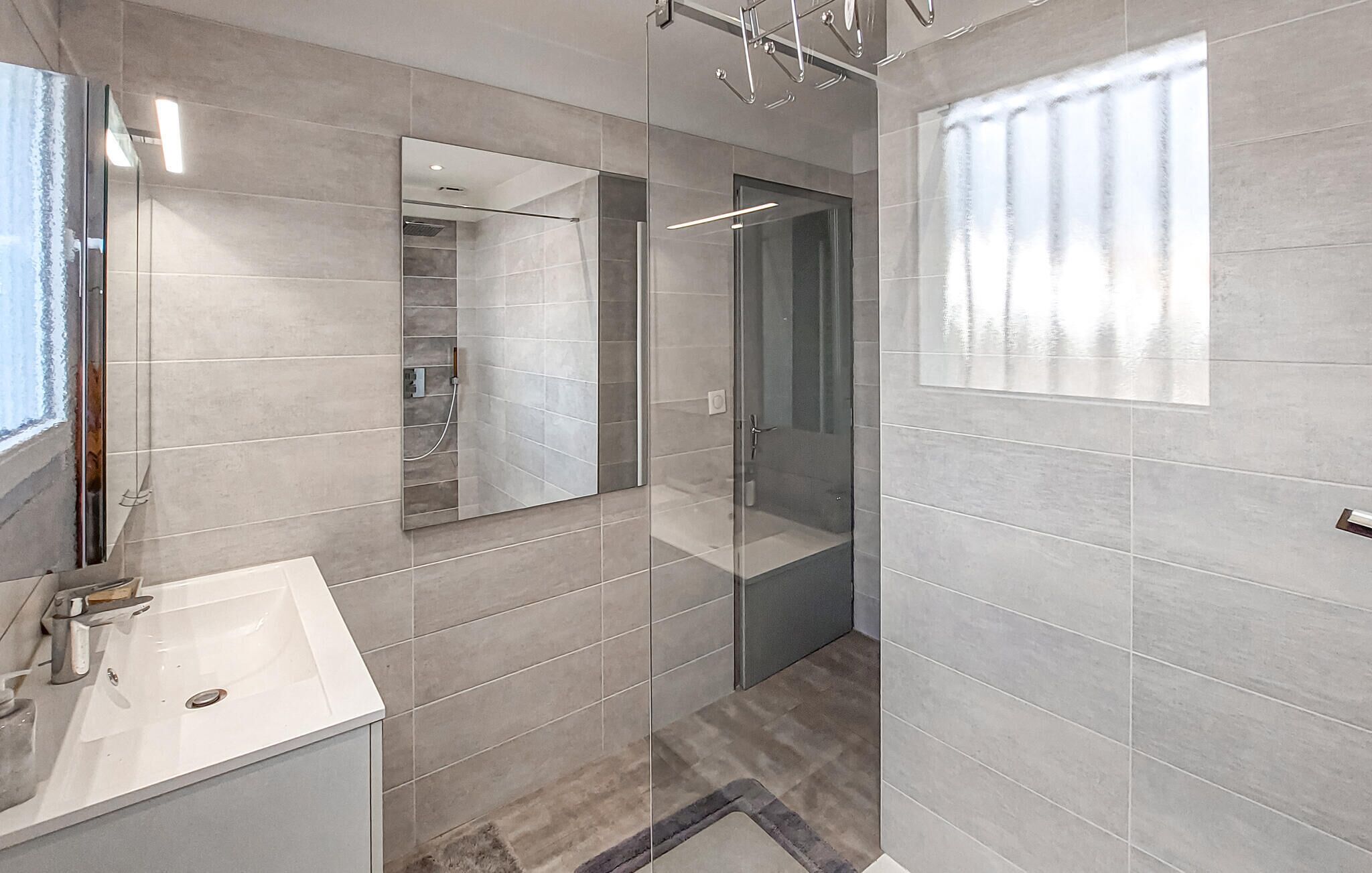 A modern bathroom with a large mirror, a sink, and a shower area.