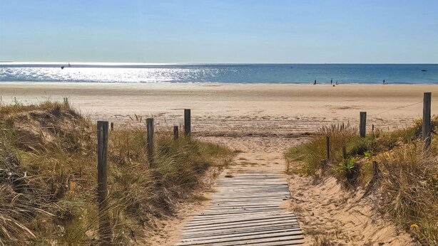 Ein hölzerner Weg führt zu einem Sandstrand mit freiem Blick auf den Ozean.