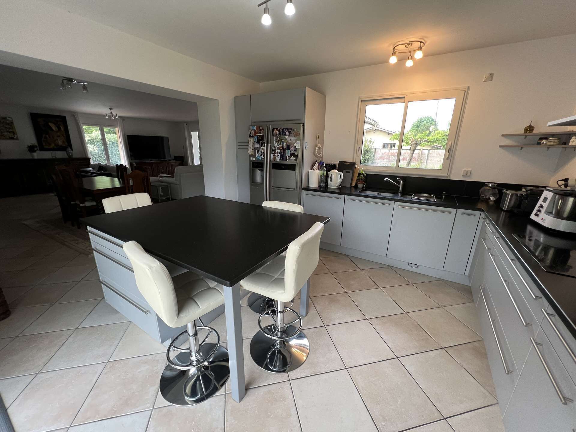 A modern kitchen with a central island, white bar stools, and a large window providing natural light.