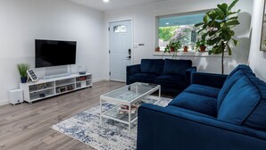Ein modernes Wohnzimmer mit einem Flachbildfernseher, zwei blauen Sofas, einem Glastisch und einer weißen Unterhaltungsanlage.