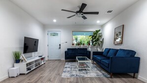 Ein modernes Wohnzimmer mit Fernseher, zwei blauen Sofas, einem Couchtisch und einem Deckenventilator.