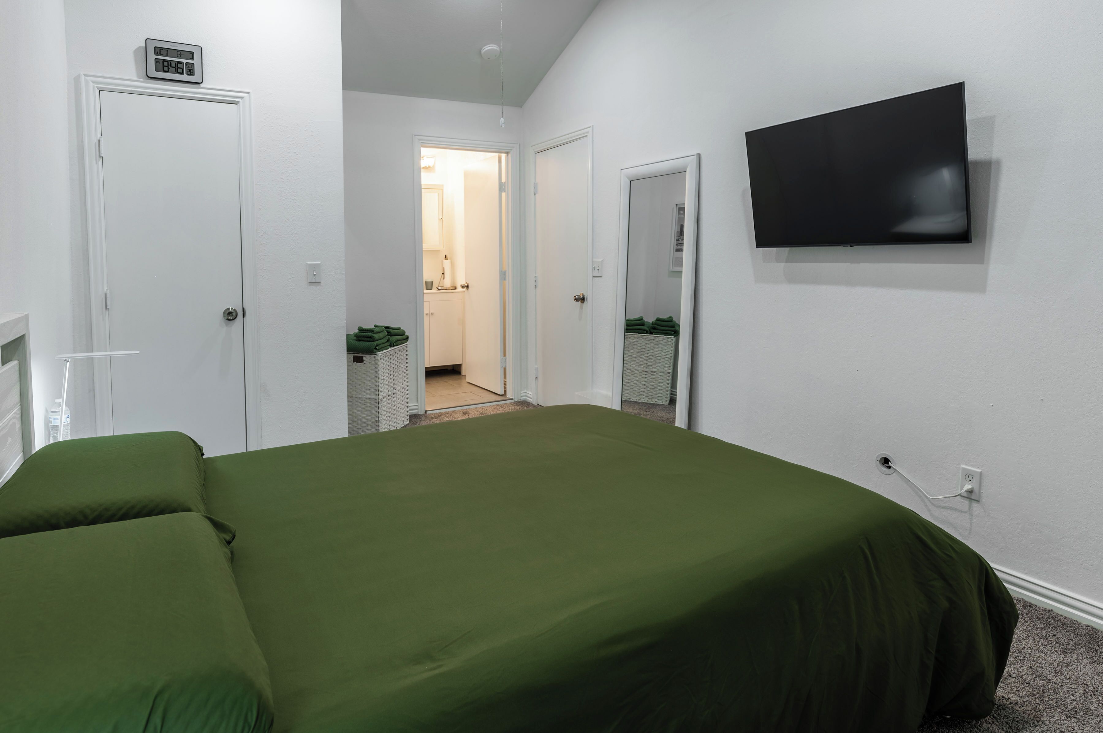 Una habitación de hotel con una cama, un televisor montado en la pared y una puerta que da a un baño.